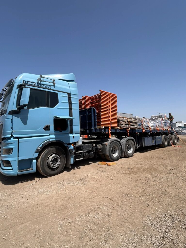 משאית עם קבינה כחולה עמוסה במסגרות מתכת כתומות